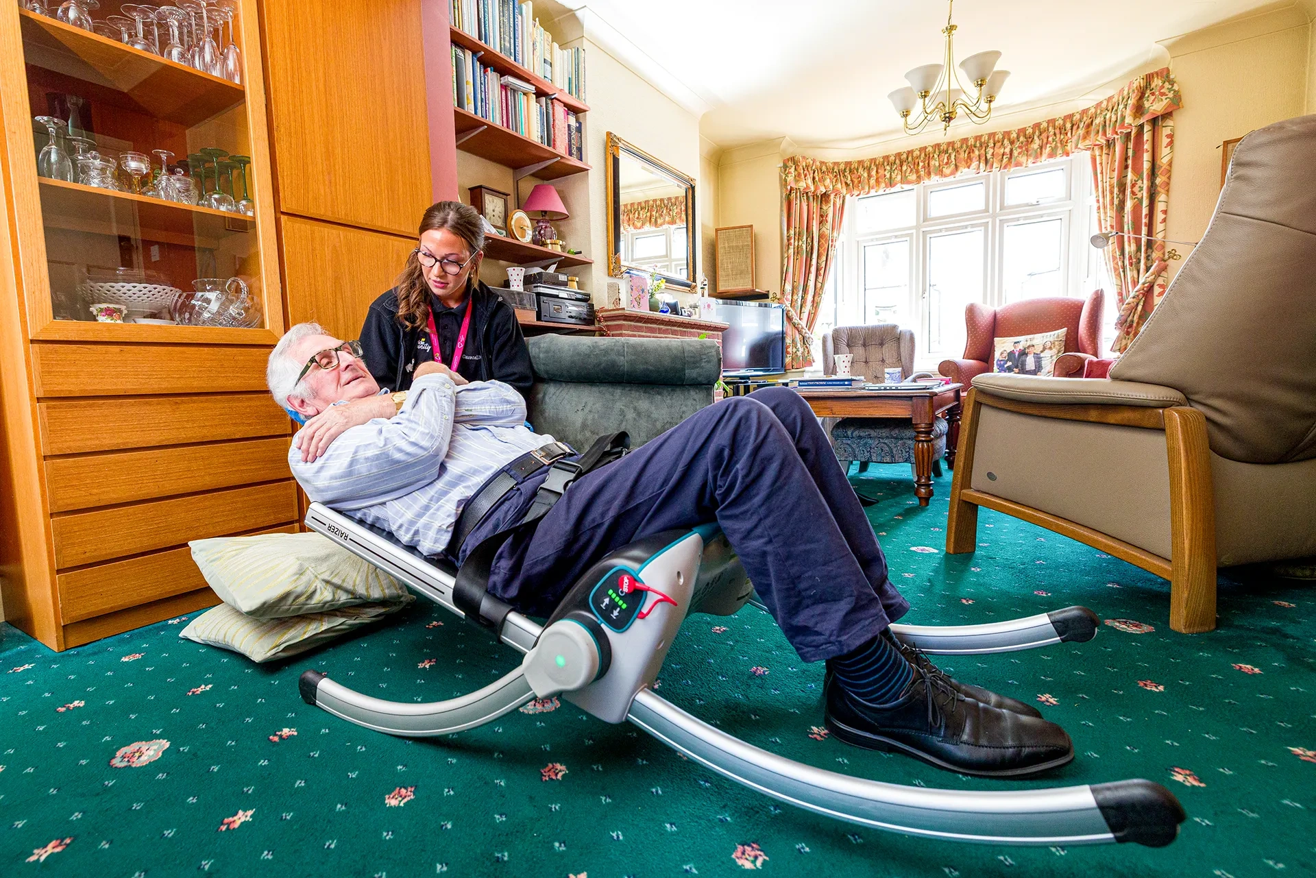 A Provide Carecall247 responder helping an older man up from the floor with a lifting chair.