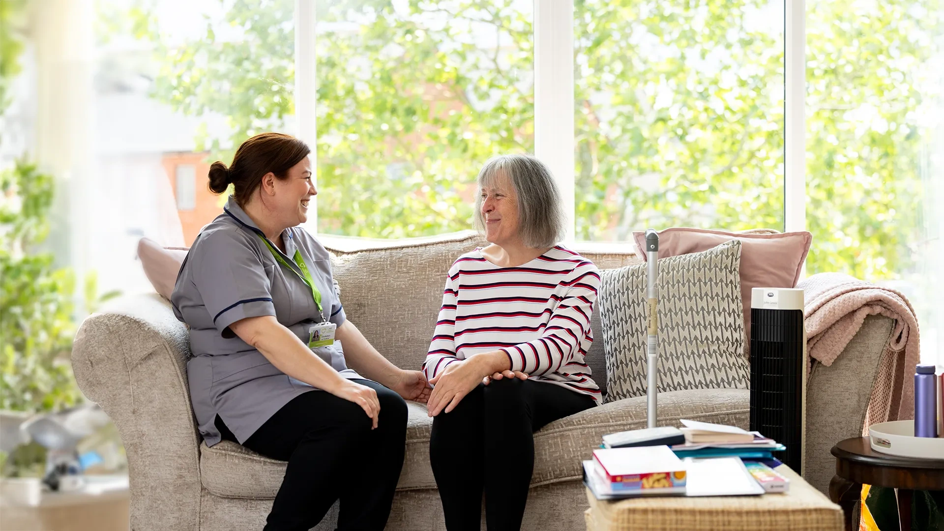 A care worker sitting and talking with an older woman on her sofa.